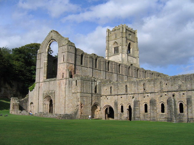 Image of Fountains Abbey, a large, stone building with very little decoration with a green lawn in the foreground.