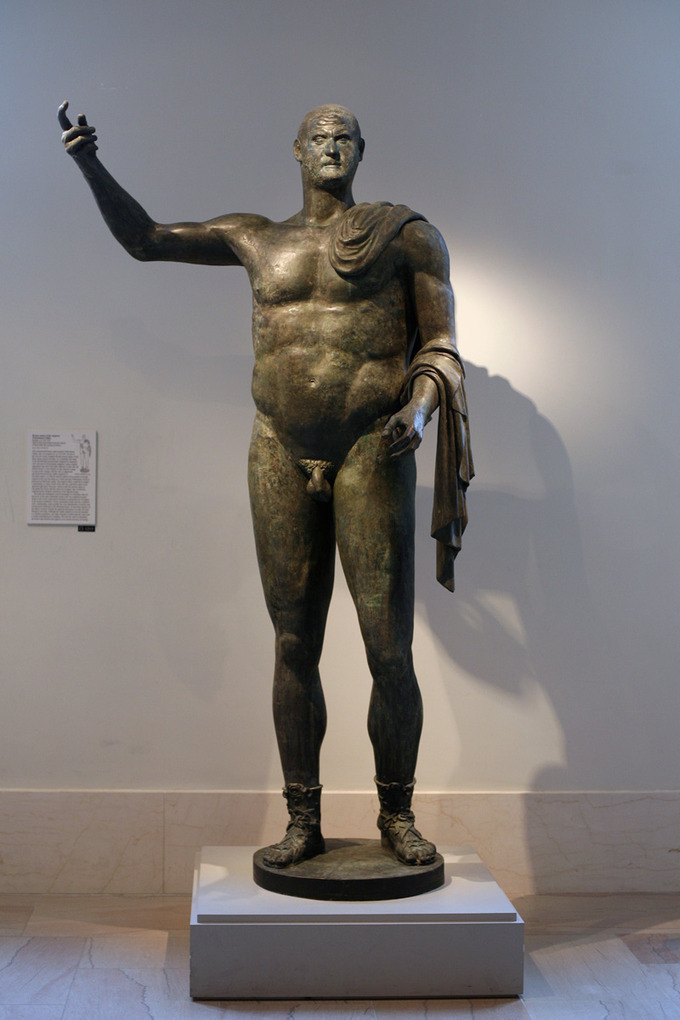 This is a photo of the statue of Trebonianus Gallus. It is a full-length standing nude statue. The body is large, bulky, and muscular. The head is disproportionately small.