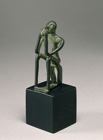 Photo shows a bronze figure, seated with its head in its hands. Its limbs are thin and elongated.