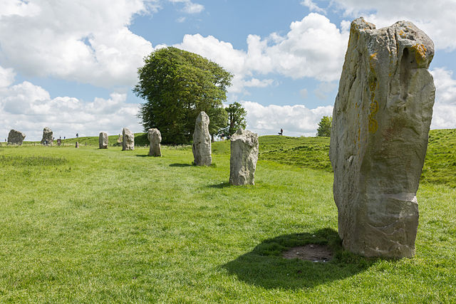 Photograph depicts stones at Avebury. Stones are arranged to form a large circle. The photo is taken at an angle that displays part of the circle.