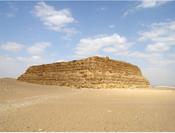 Color photograph depicts flat-roofed, rectangular structure with inward sloping sides, constructed out of mud-bricks.