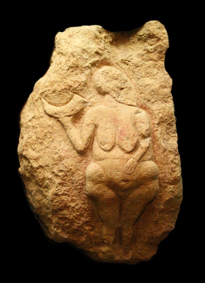 Photograph depicts limestone carving of a nude woman. The figure holds a bison horn, or possibly a cornucopia, in one hand.