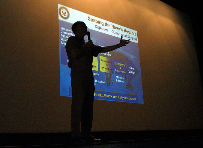 Commander Naval Reserve Force, Vice Adm. John G. Cotton, stands in front of a PowerPoint presentation at the Naval Station North Island's theater.
