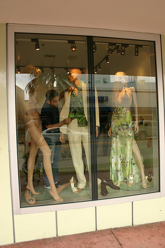 A retail store worker dresses mannequins in a store window.