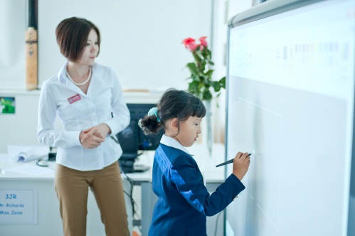 A teacher watches as a student writes on a dry erase board.