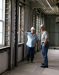 Two engineers in hard hats stand inside a building that's under construction and discuss the work.