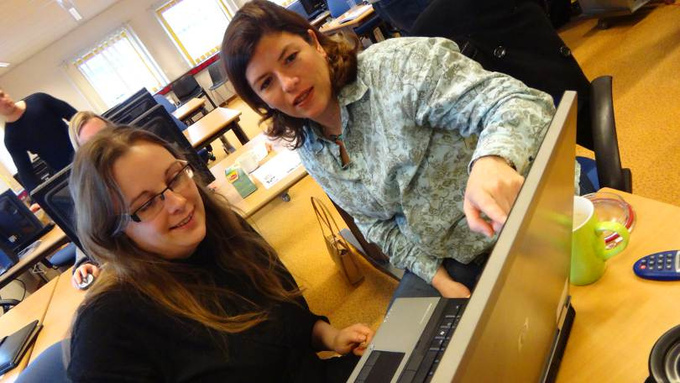 Two women look at a laptop and discuss information that is on the screen.