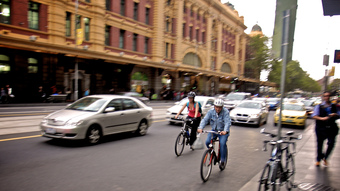 A man and woman ride bicycles in traffic.