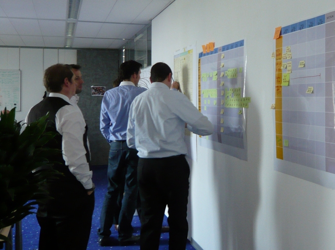 A group of businessmen work on a series of plans that are displayed on an office wall.