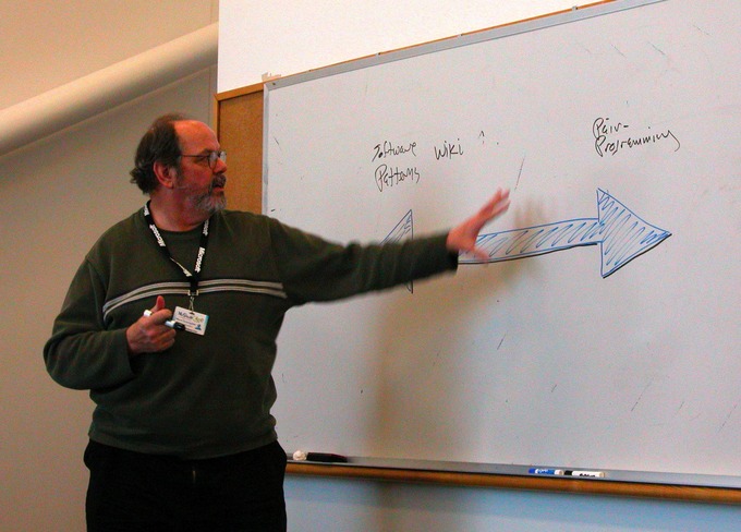 A man gives a presentation and discusses information on a dry erase board.