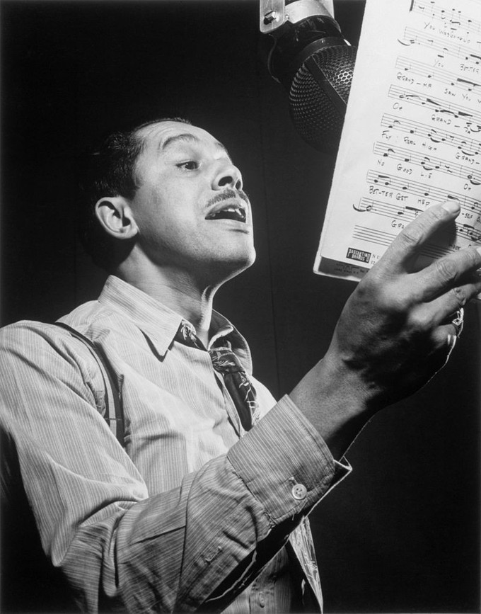 Portrait of Cab Calloway singing into a microphone while holding sheet music.