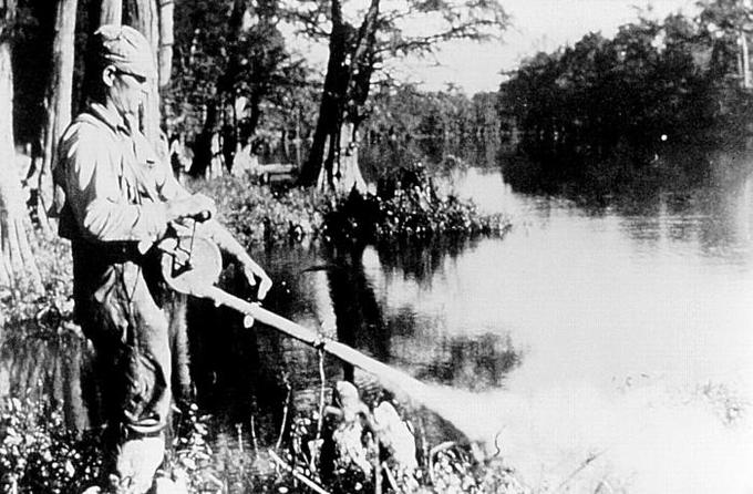 A photograph of a man spraying DDT on the bank of a river.