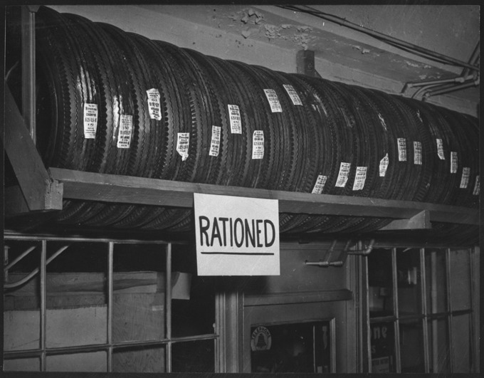 The black and white photograph shows a shelf of Firestone tires. A sign that says 
