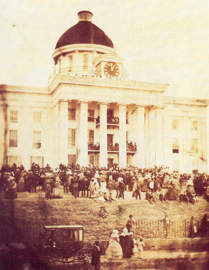 The photograph depicts a large crowd of people gathered in front of the Alabama capitol building.