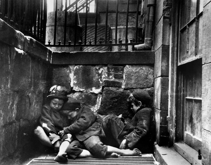 The photograph shows three poor children without shoes sleeping huddled up against each other in the street.