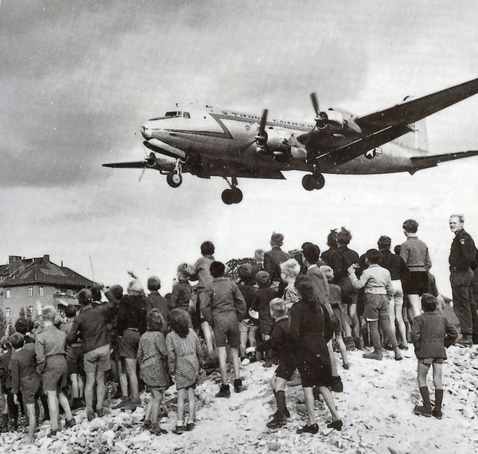 Photo of a group of people watching a plane land during the Berlin airlift.
