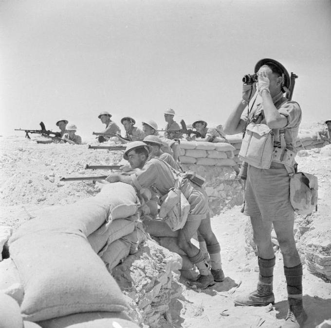 Image of armed British soldiers lined up against a wall of sandbags in the Alamein, Egypt.