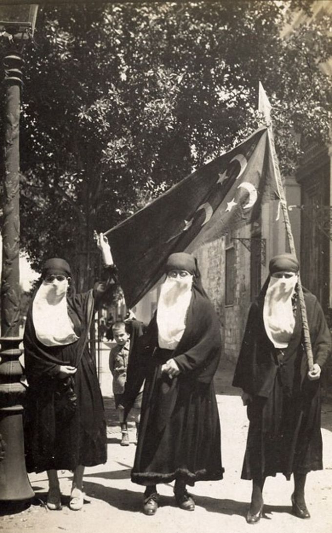 Image of Egyptian women wearing black dresses, black head covers, and white veils over their faces, carrying an Egyptian glad, demonstrating against British occupation during the revolution of 1919.