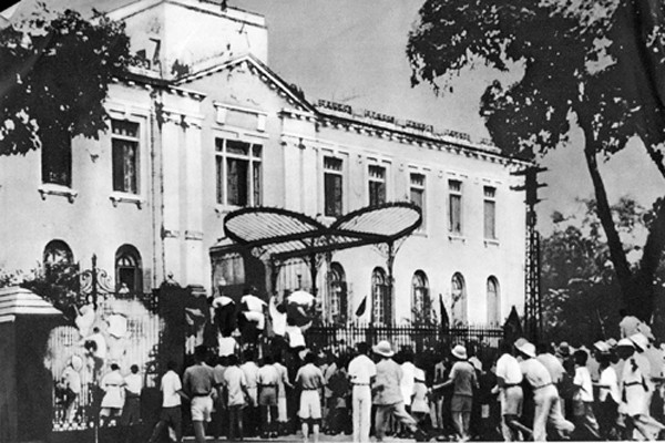 The photograph shows a crowd gathered at the gates of a government building.