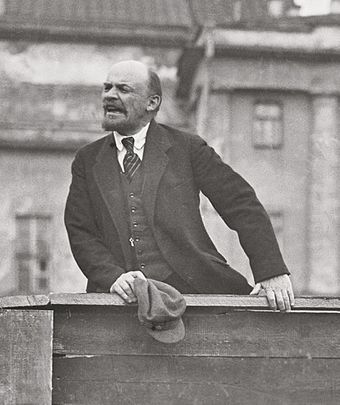 A photo of Vladimir Lenin speaking from atop a wooden platform.