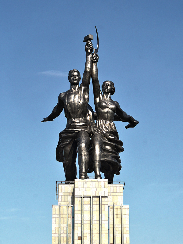 A photo of a Soviet era statue characteristic of socialist realism, depicting a male worker holding a hammer aloft in his hand and a woman worker with a sickle aloft in her hand.