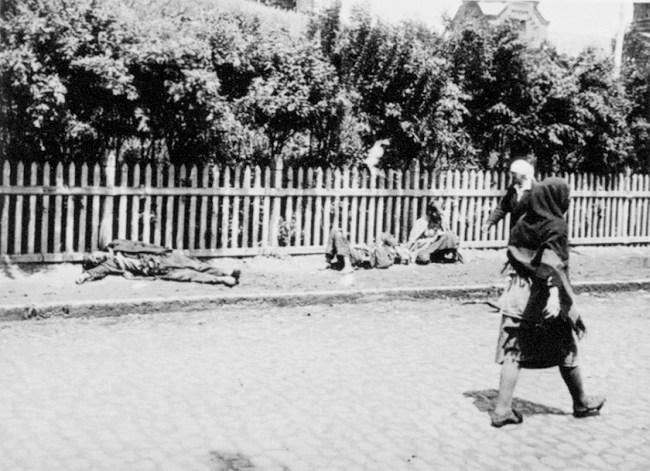 Photo of a street in the Ukraine with several people lying dead or dying and several others walking by.