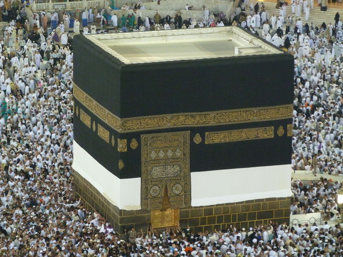 A photo of the Kaaba, a black cube worshipped by Muslims, surrounded by people.
