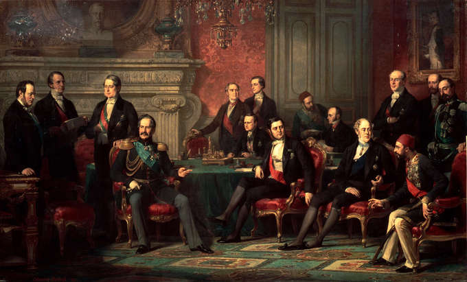 The painting depicts 15 men sitting and standing around a lavish parlor room.