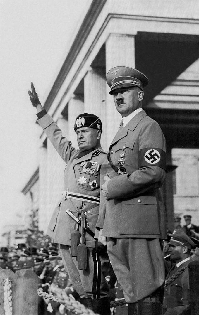 Photo of Hitler and Mussolini in official military uniforms overlooking a crowd of people.