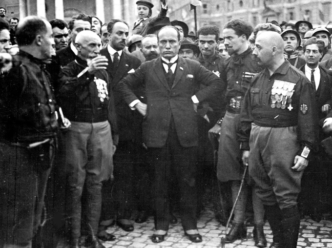 A photo of a crowd of mostly men, with Mussolini and other fascist leaders in the center.