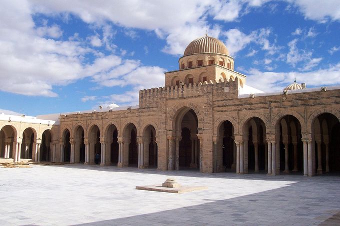 A photo of a large mosque and a courtyard, characterized by arches and pillars and a dome in the center.