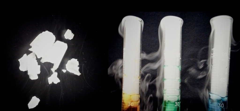 This figure shows pieces of a white substance which appear to be sublimating. To the right of these pieces are three graduated cylinders. Each cylinder holds a different color liquid, and above the liquid, the cylinders are filled with a fog-like substance. This fog-like substance swirls out of the top and around the outside of the cylinders.