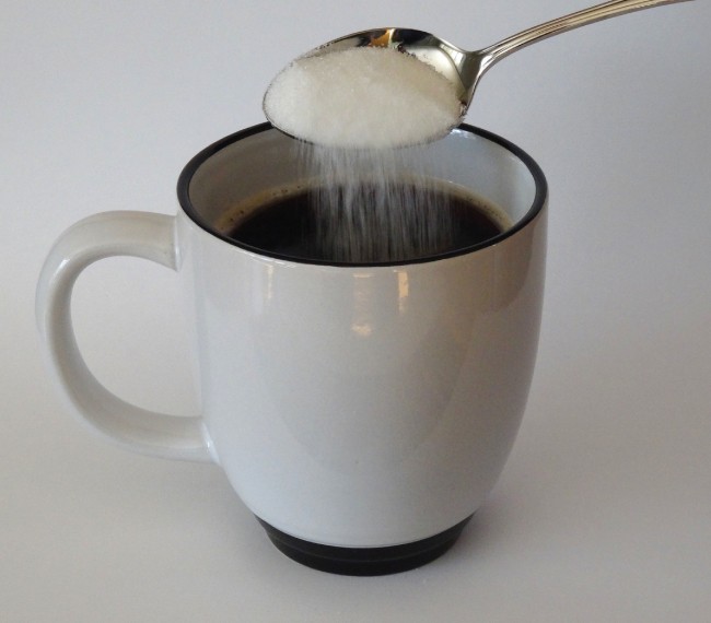 A picture is shown of sugar being poured from a spoon into a cup.
