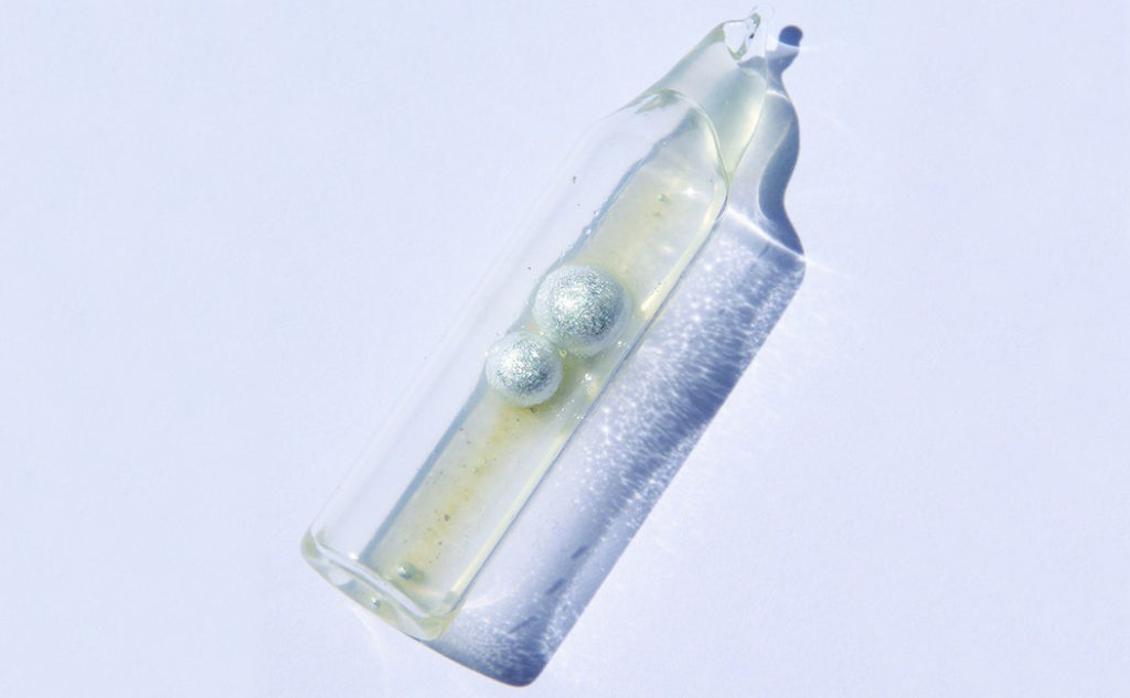 A sealed, tube-like glass container is shown. The container is partially filled with a colorless liquid and contains two metallic spheres.