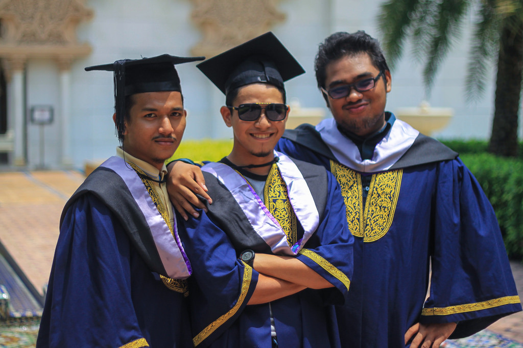 Photo of three young men with their arms around one another, smiling, in graduation caps and gowns.