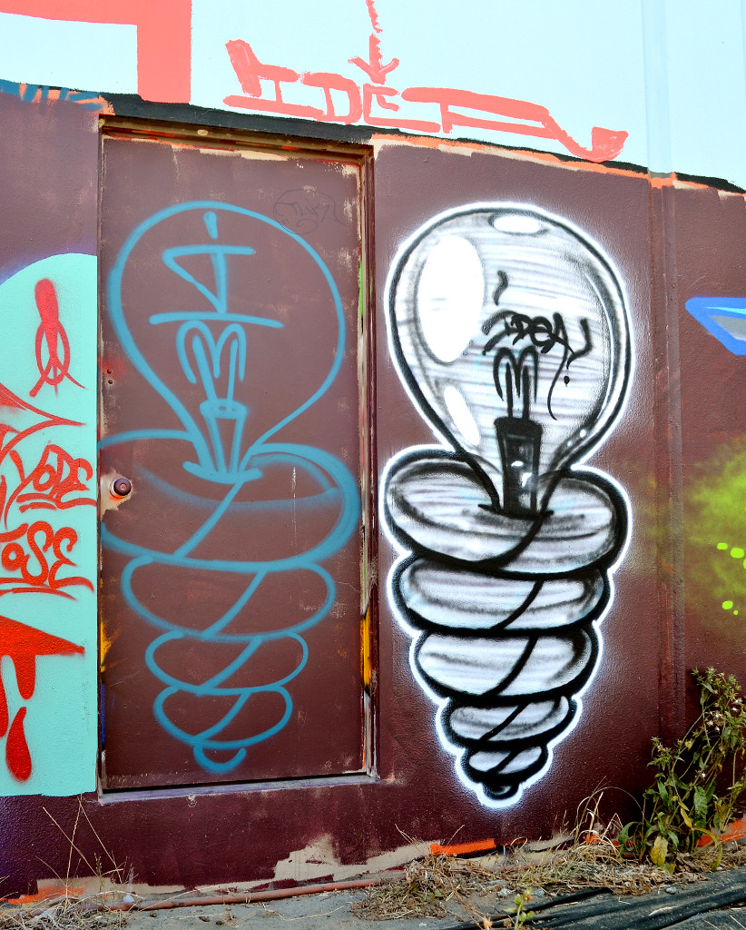 Photo of colorful graffiti on a door and wall, showing two lightbulbs and the word 