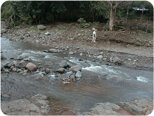 A person walking along the bed of a river. There are many rocks on the riverbed.