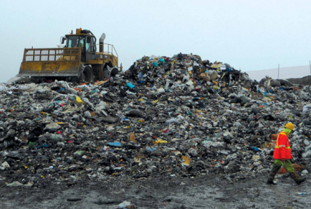 A man walks by a large pile of garbage and debris that is twice as tall as he is.