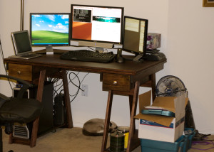 A desk with three computer monitors atop it and a cat sleeping below it.
