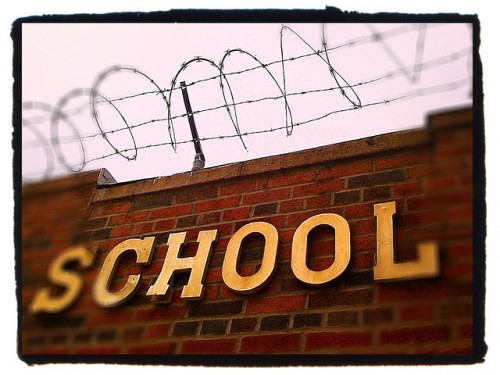 A brick wall is shown with the word “school” on it and barbed wire on top.