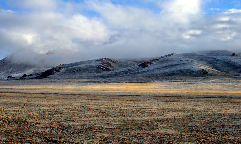 A frosty ground with very low brown vegetation. Mountains rise up along the horizon