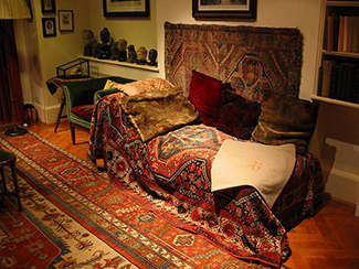 This photograph shows what Freud’s famous psychoanalytic couch looked like. The couch is draped in tapestries and pillows, and the room is decorated with sculptures, books and pictures on the wall. (Prochaska & Norcross, 2010). (credit: Robert Huffstutter)