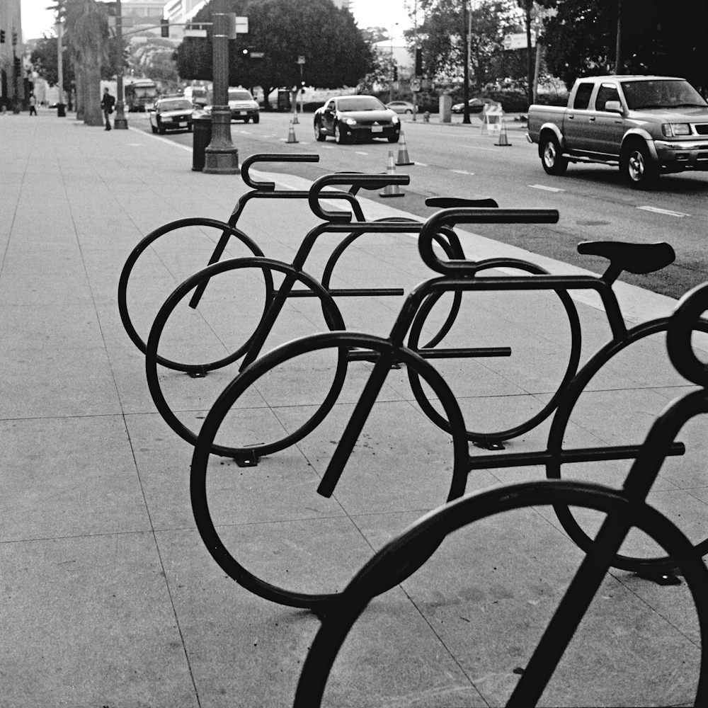 Black-and-white photo of four bicycle-shaped bike racks on a city thoroughfare.
