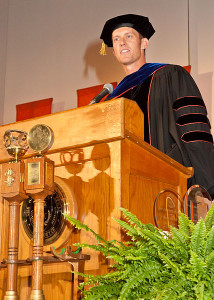 Photo of a man in a graduation gown standing at a lectern