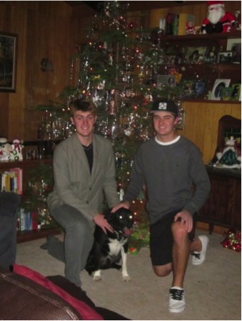 Photo of two teenage boys kneeling in front of a Christmas tree, with a dog between them