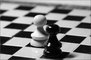 Black and white photo of two pawns, one white and one black, diagonal from one another on a chessboard