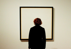 Photo of a woman staring at an empty frame hanging on a wall