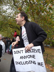 Man holding a sign that says Don't believe anyone, including me.