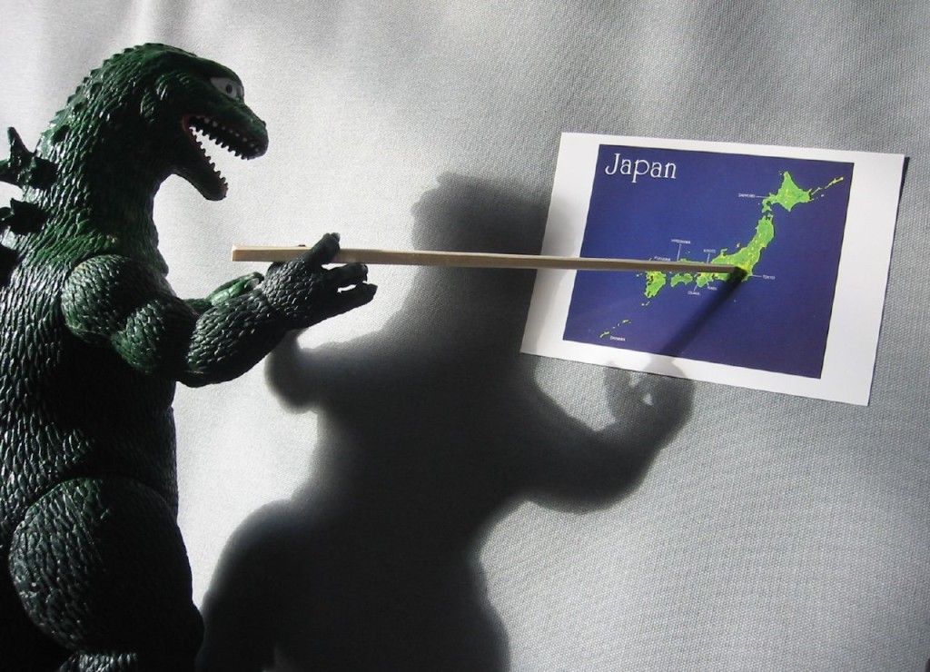 A Godzilla figurine holding a stick that points to a map of Japan.