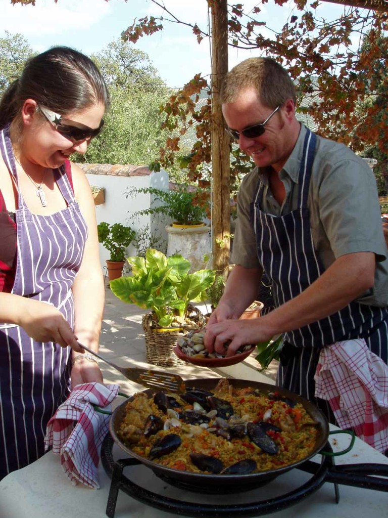 A man and woman cooking paella outdoors in Spain.